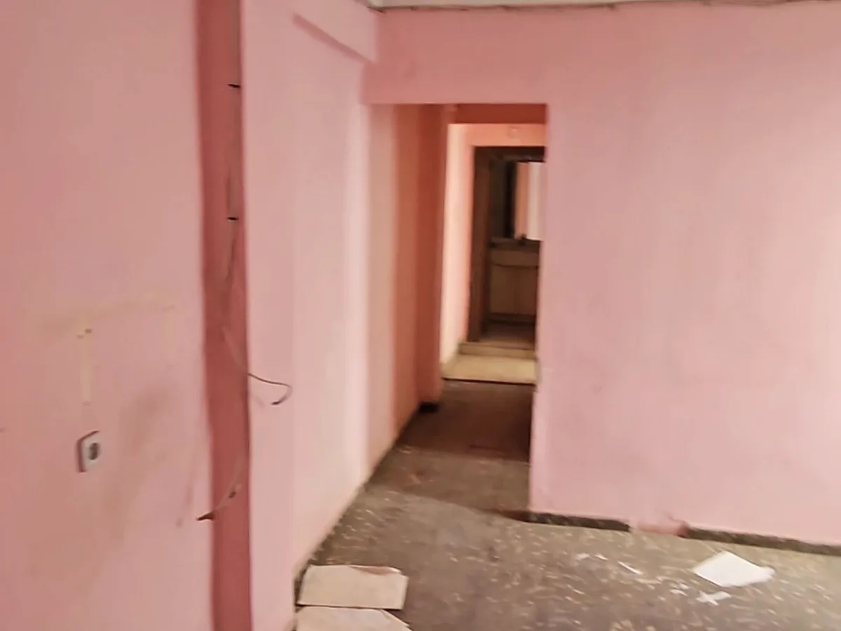 Distribuidor de la vivienda antes de la reforma, con paredes originales y suelo por retirar