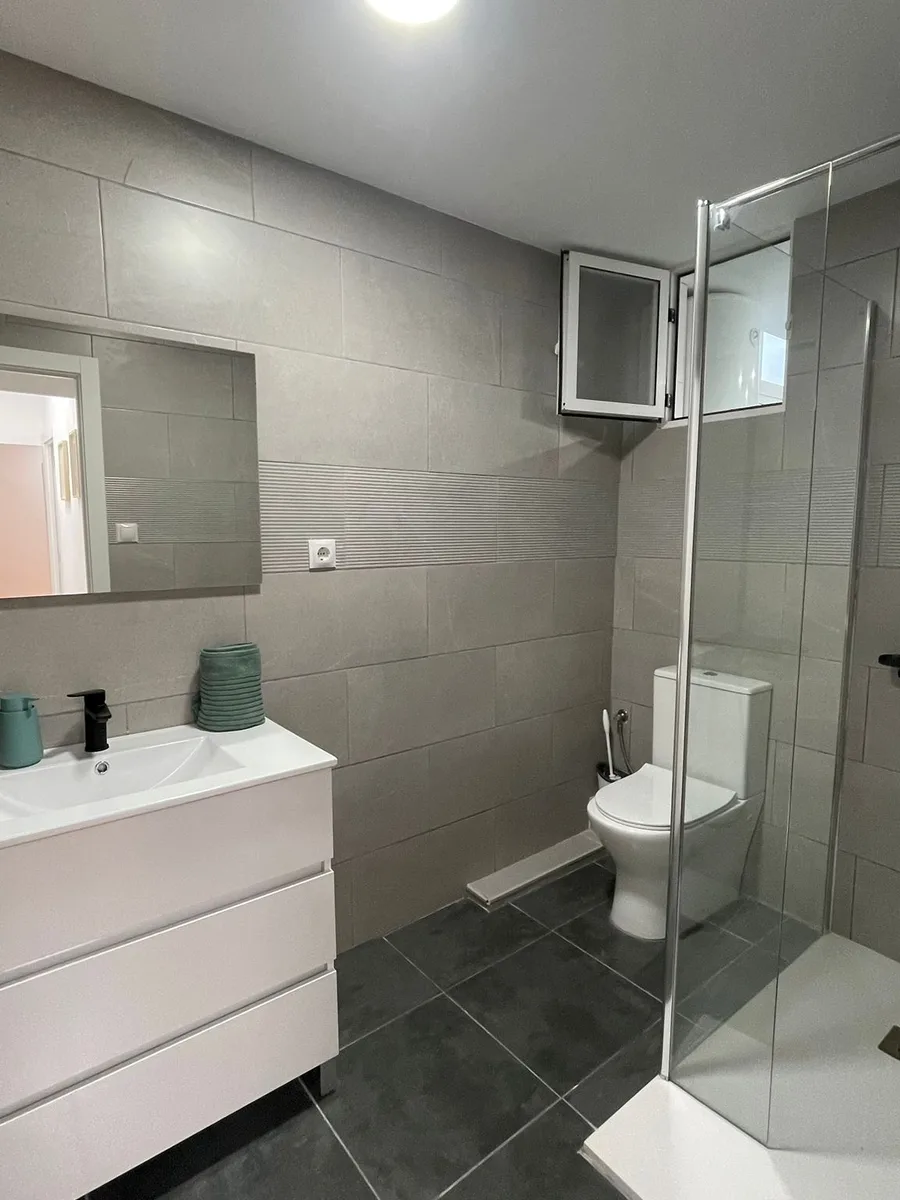 Baño reformado en Catarroja con azulejo gris, mueble suspendido y ducha de obra