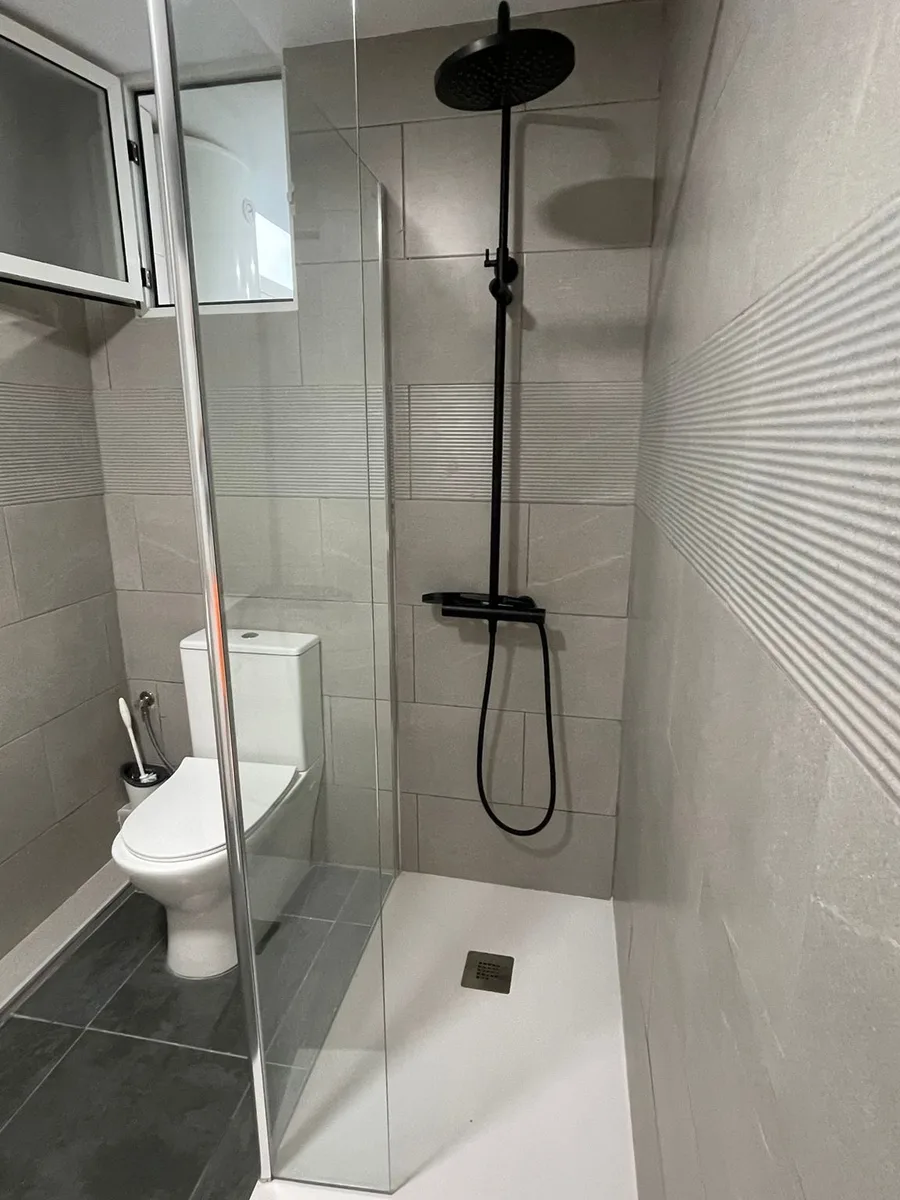 Ducha de obra con mampara de cristal y grifería negra en Catarroja